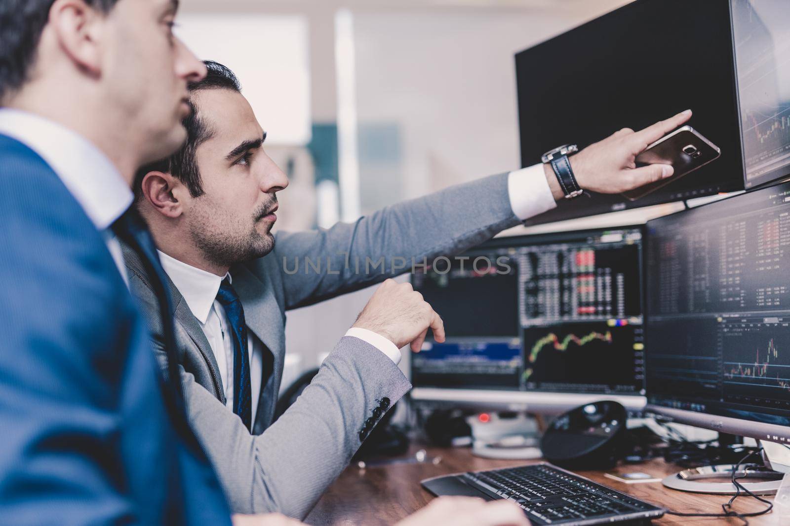 Businessmen trading stocks online. Stock brokers looking at graphs, indexes and numbers on multiple computer screens. Colleagues in discussion in traders office. Business success concept.