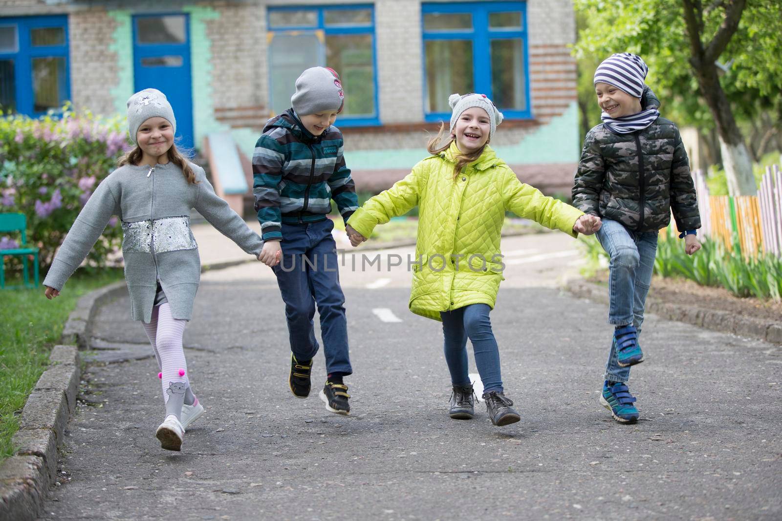 Belarus, the city of Gomel, May 10, 2019. Open day in kindergarten.Happy preschoolers on the street. Children holding hands jumping. A group of six year old friends. by Sviatlana