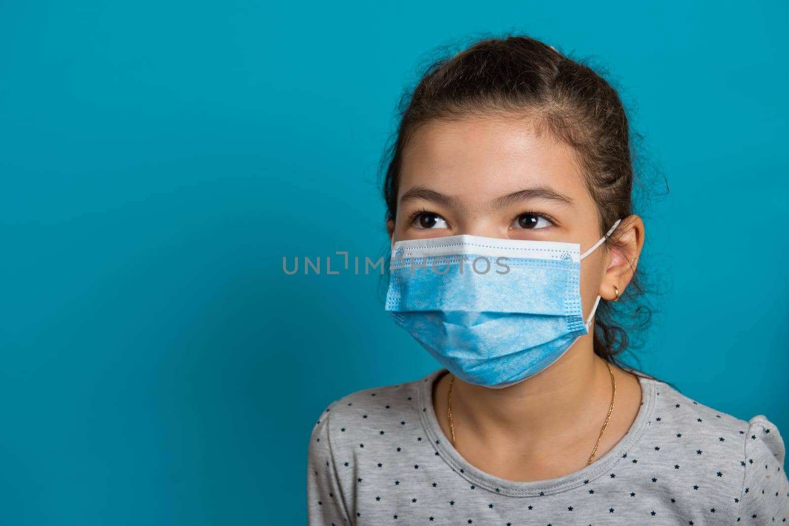 Arabian small girl in medical mask on blue background. Close-up. 