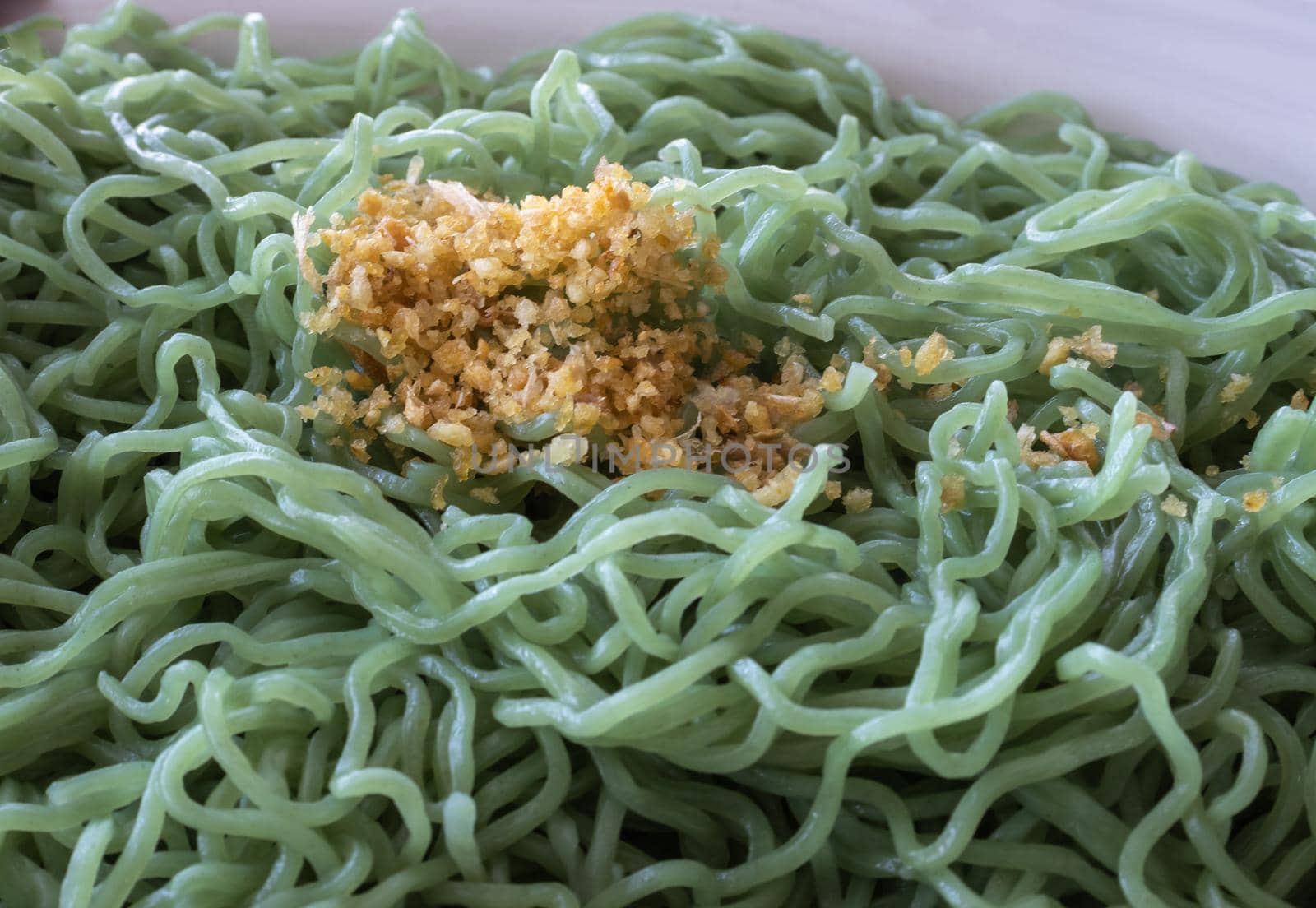 Green noodles sprinkled on top with fried garlic, taken close-up.