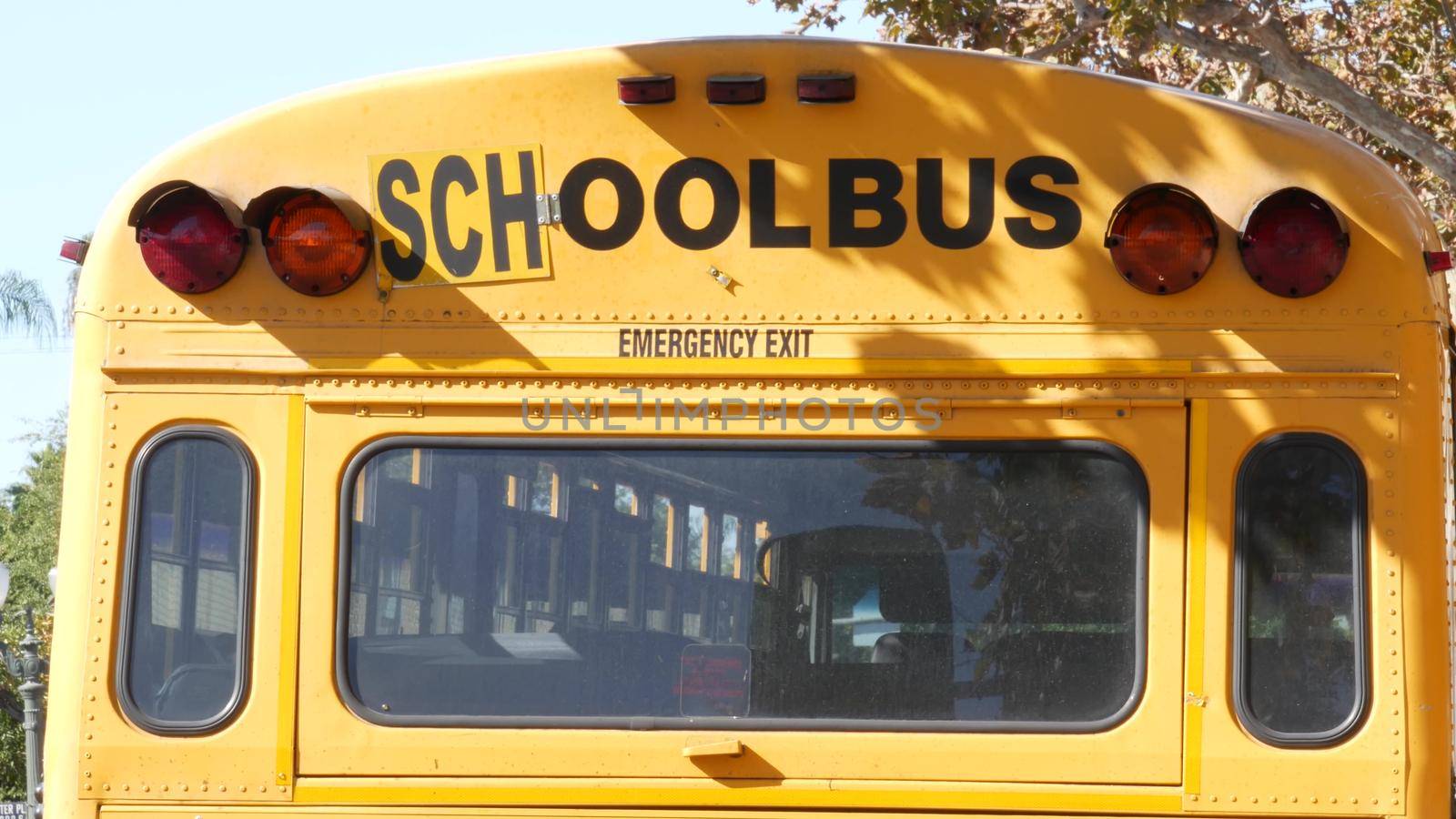 Yellow iconic school bus in Los Angeles, California USA. Classic truck for students back view. Vehicle stoplights for safety of children transportation. Public passenger transport for kids in suburb.