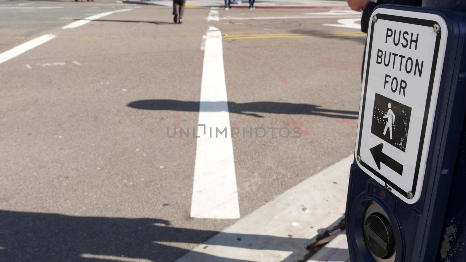 Traffic light button on pedestrian crosswalk, people have to push and wait. Traffic rules and regulations for public safety in USA. Zebra street crossing on road intesection in San Diego, California.