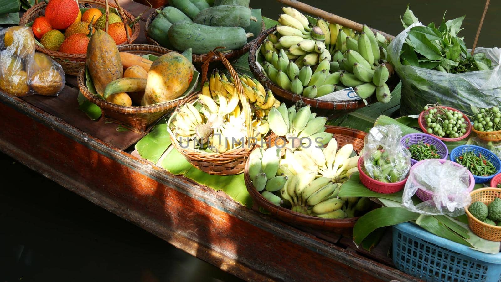 Iconic asian Lat Mayom floating market. Khlong river canal, long-tail boat with tropical exotic colorful fruits, organic locally grown vegetables. Top view of harvest and street food in wooden canoe.