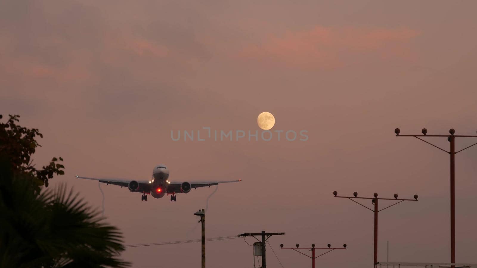 Airplane landing in LAX airport at sunset, Los Angeles, California USA. Passenger flight or cargo plane silhouette, dramatic cloudscape. Aircraft arrival to airfield. International transport flying by DogoraSun