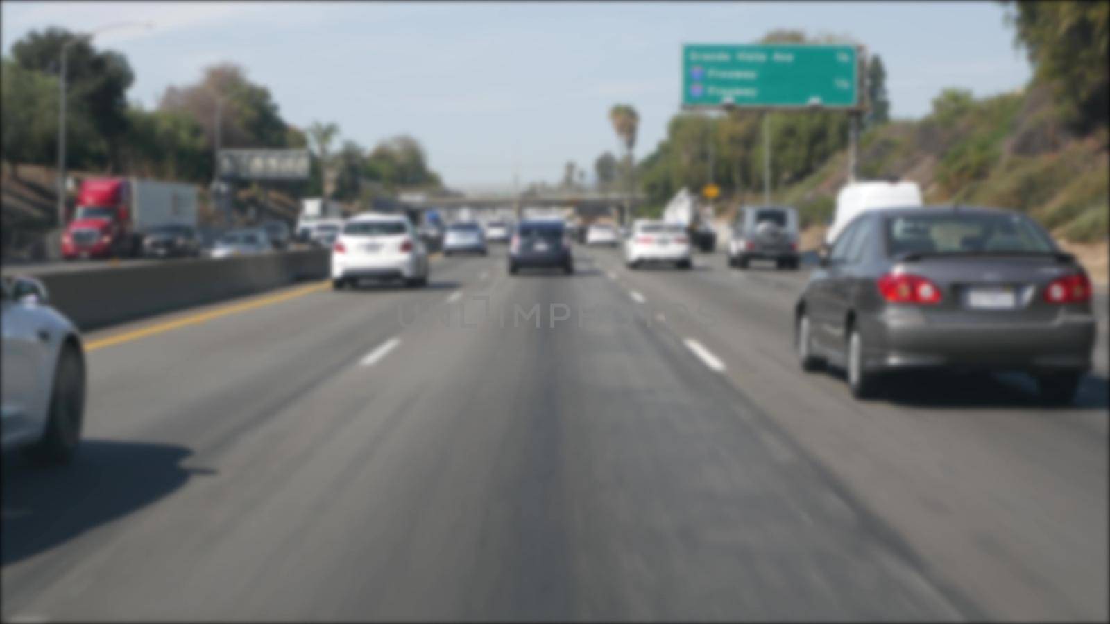 Driving on intercity freeway in Los Angeles, California USA. Defocused view from car thru glass windshield on busy interstate highway. Blurred suburb multiple lane driveway. Camera inside auto in LA.