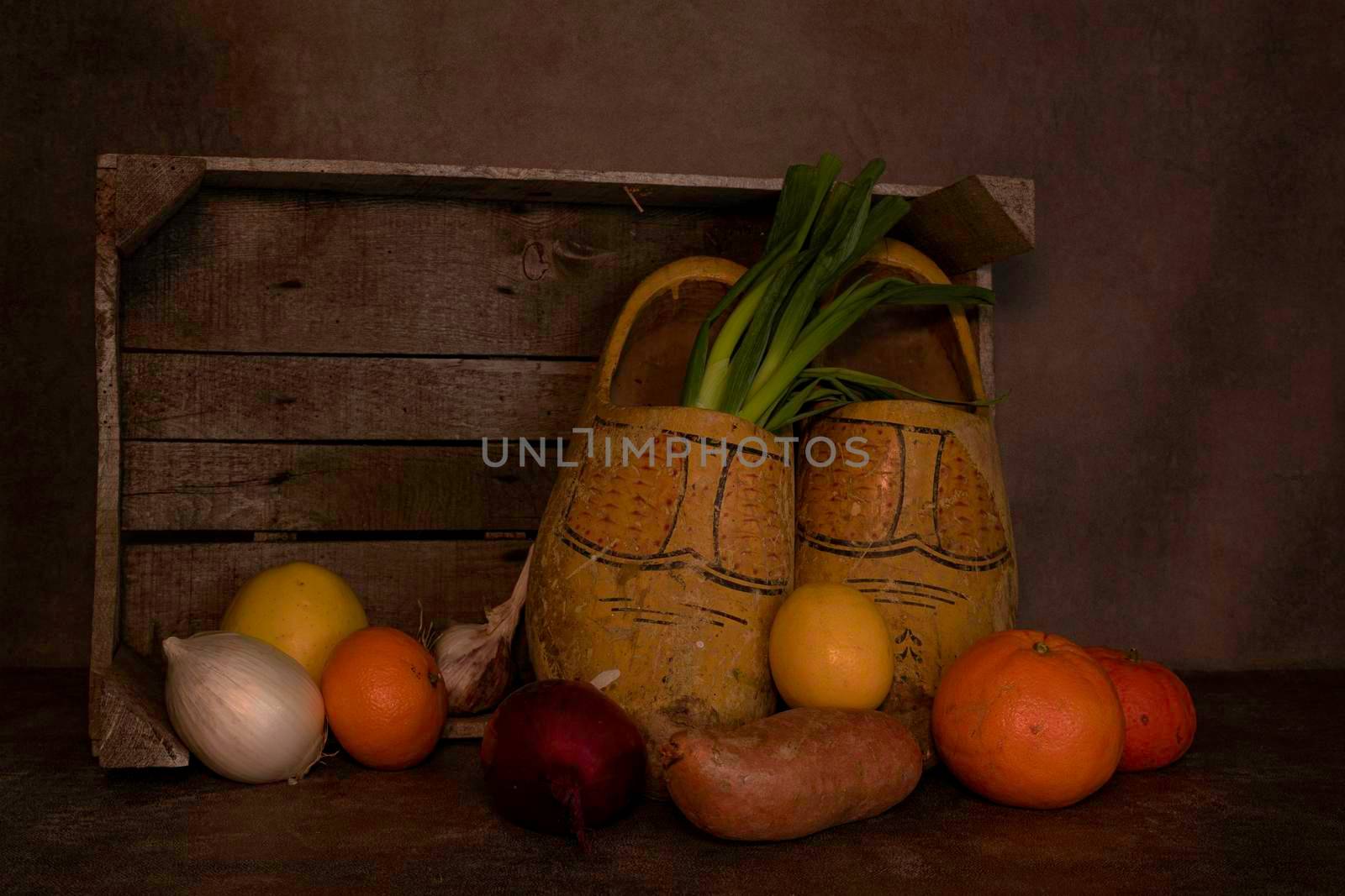 still life with a wooden box with old dutch worn out wooden shoes and various fruits