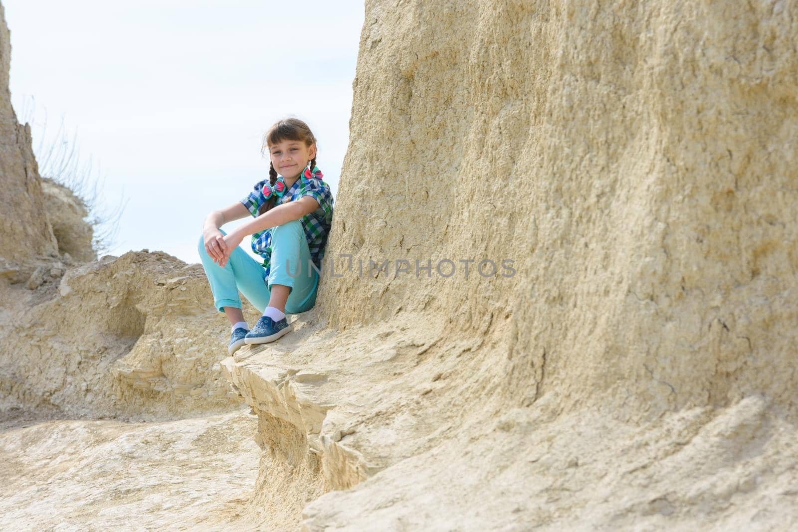 Girl in casual clothes sits on a cliff ledge