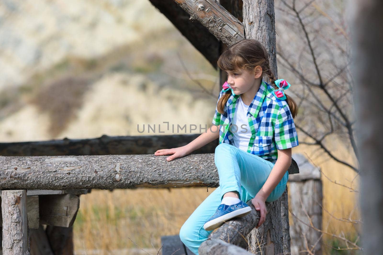 A girl tries to sit on a fence made of a thick wooden frame