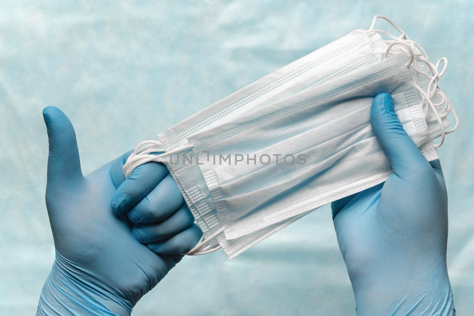 Doctor holding lot medical face mask in hands in blue medical gloves and showing thumb up. Pandemic insurance, grippe, airborne diseases, SARS. Antivirus masks for human cover mouth and nose. Concept.
