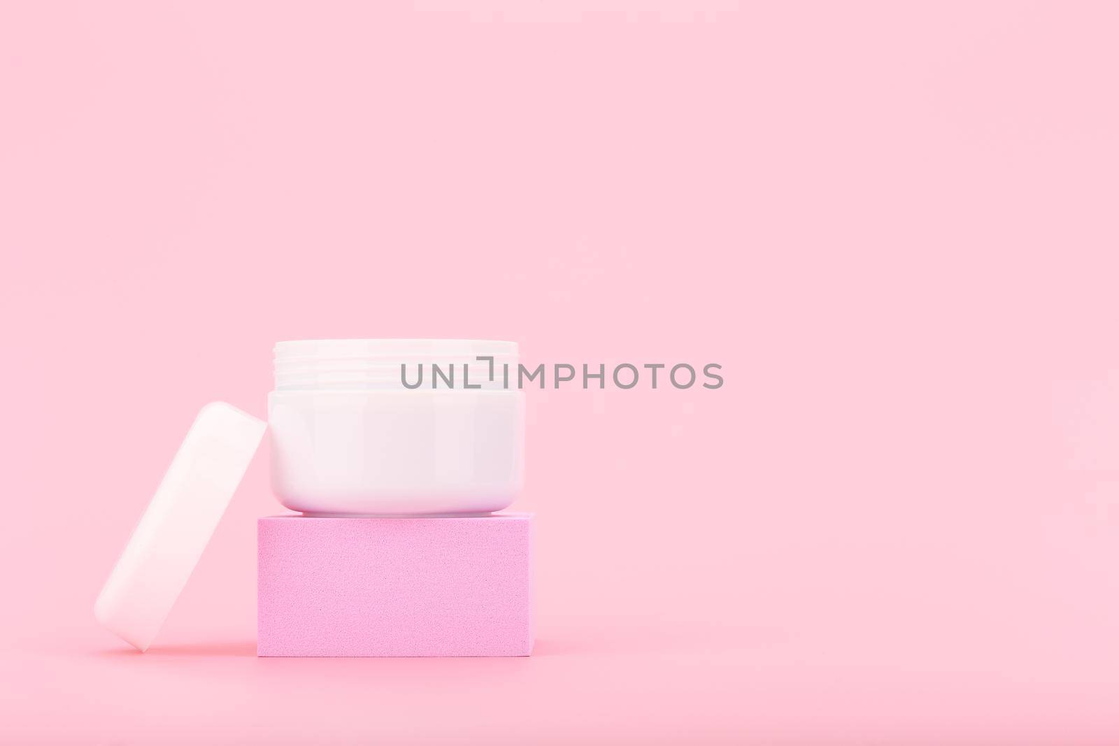 White opened cosmetic jar with cream, scrub or mask for face or hair on pink pedestal against pink background with copy space. Beauty products concept
