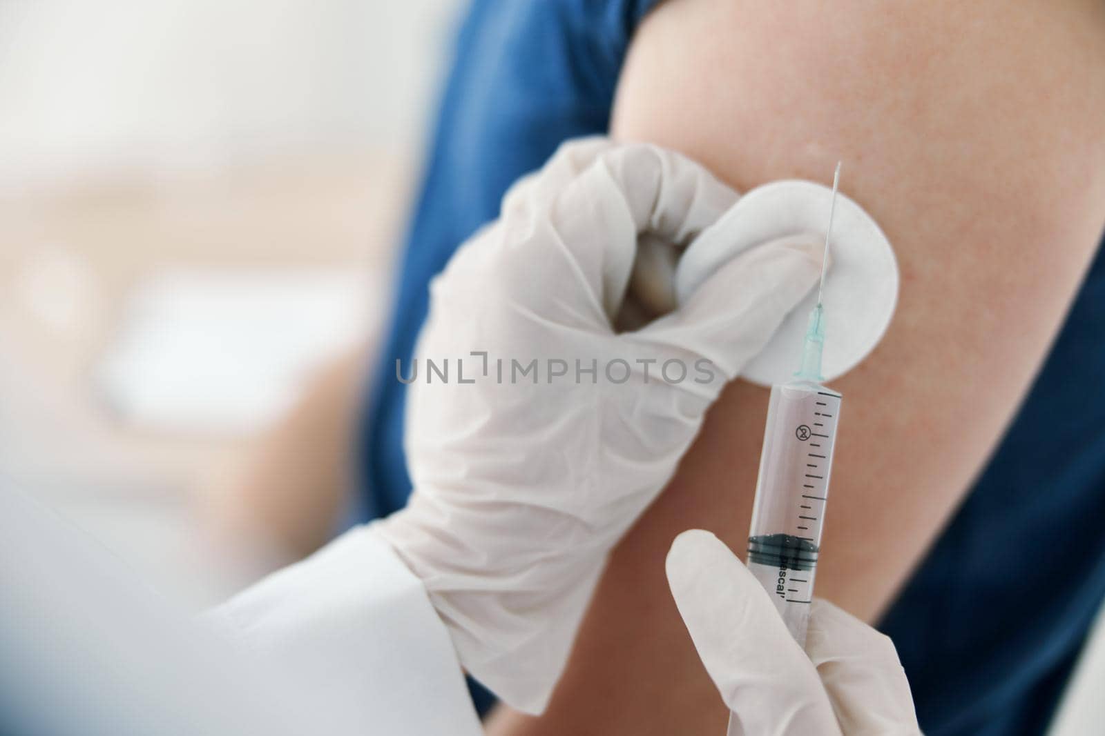 doctor holds a syringe near the patient's hand and protective gloves in a cotton pad covid vaccination by SHOTPRIME