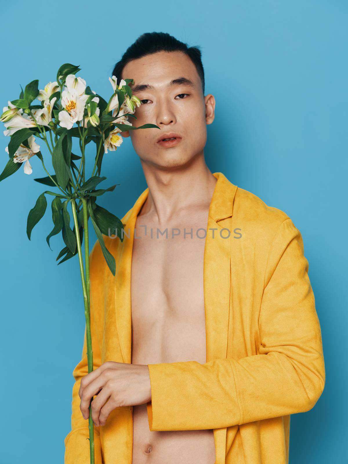 Sexy man with a naked body on a blue background and a yellow coat with a bouquet of flowers in the holidays gifts by SHOTPRIME