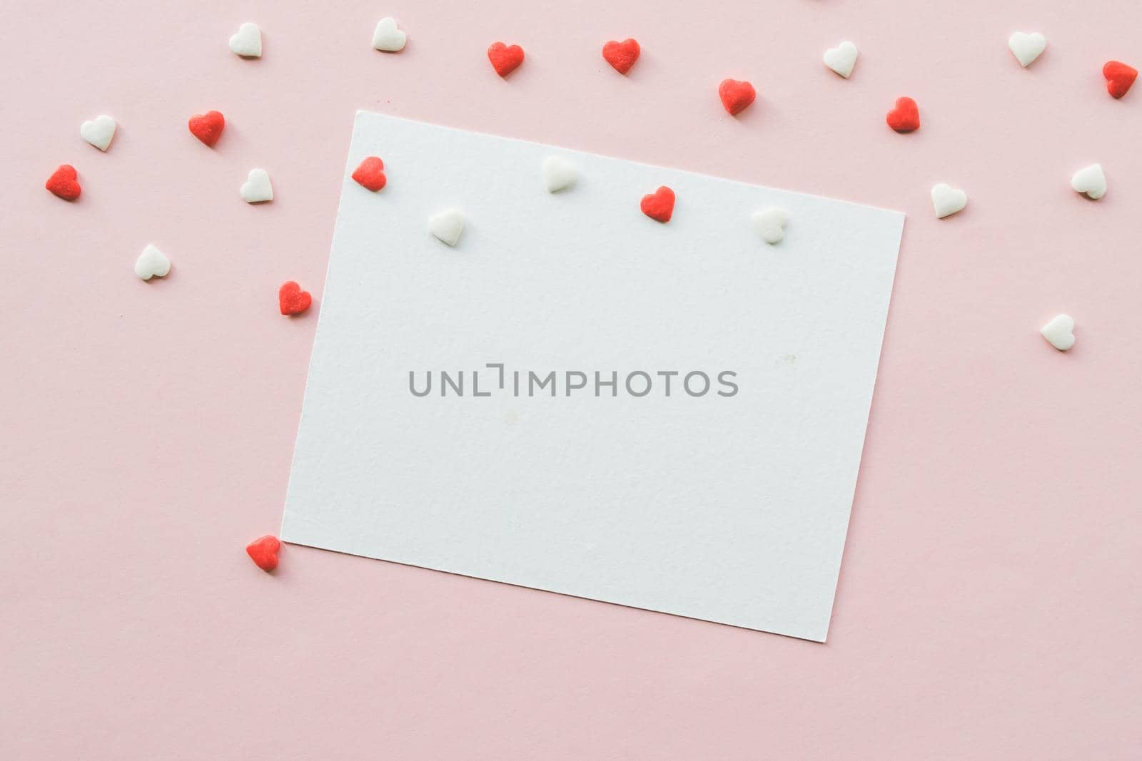 Valentine's Day background with red and white little hearts, empty white greeting card on pink backdrop. Valentines day concept. Copy space. Top view. Mockup