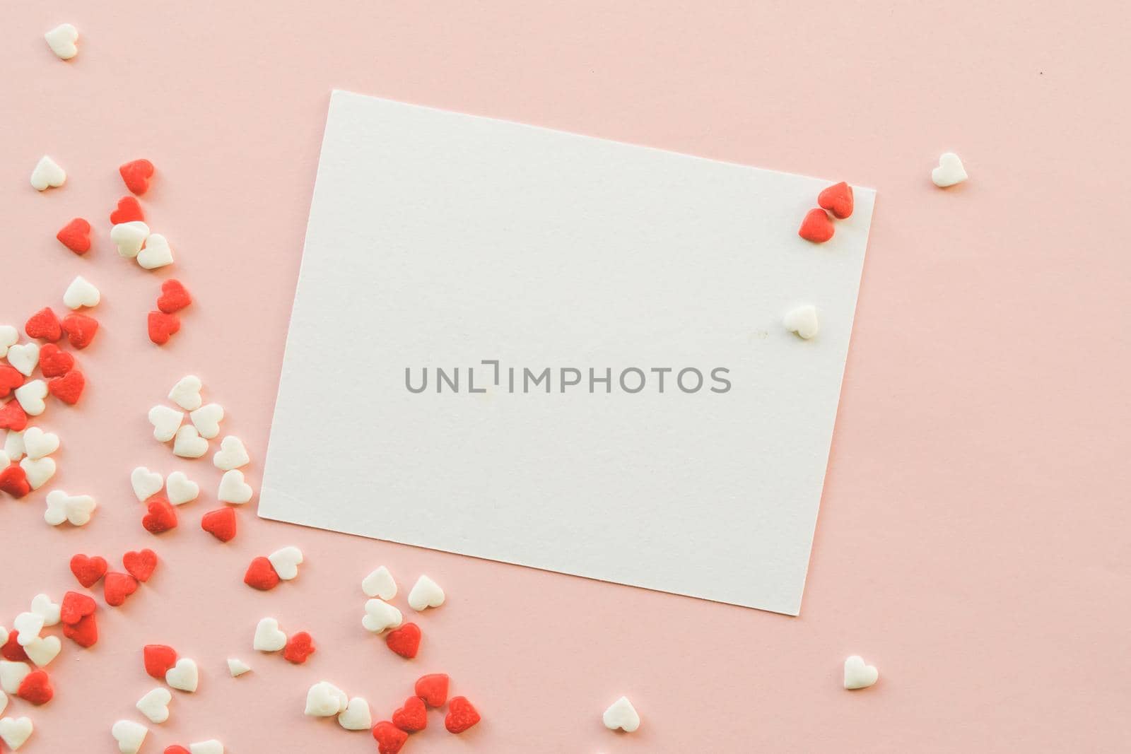 Valentine's Day background with red and white little hearts, empty white greeting card on pink backdrop. Valentines day concept. Copy space. Top view. Mockup