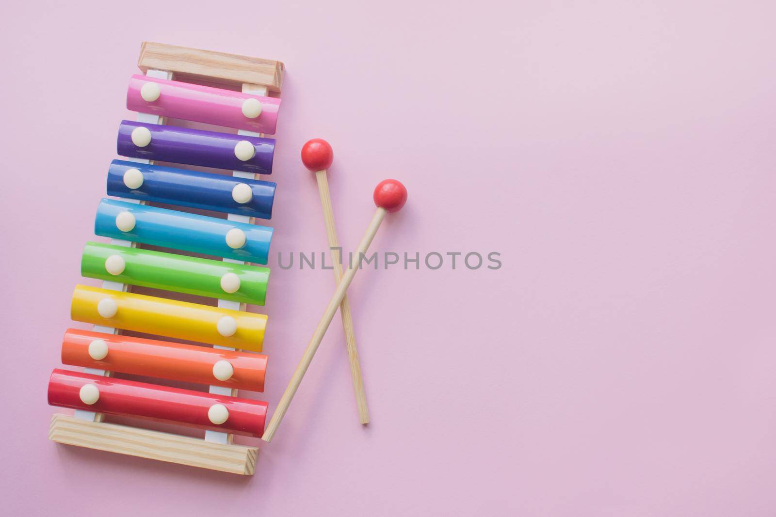 Rainbow Colored Wooden Toy Xylophone on pink bacground. Glockenspiel toy made of metal and wood. Top view. Free space for text