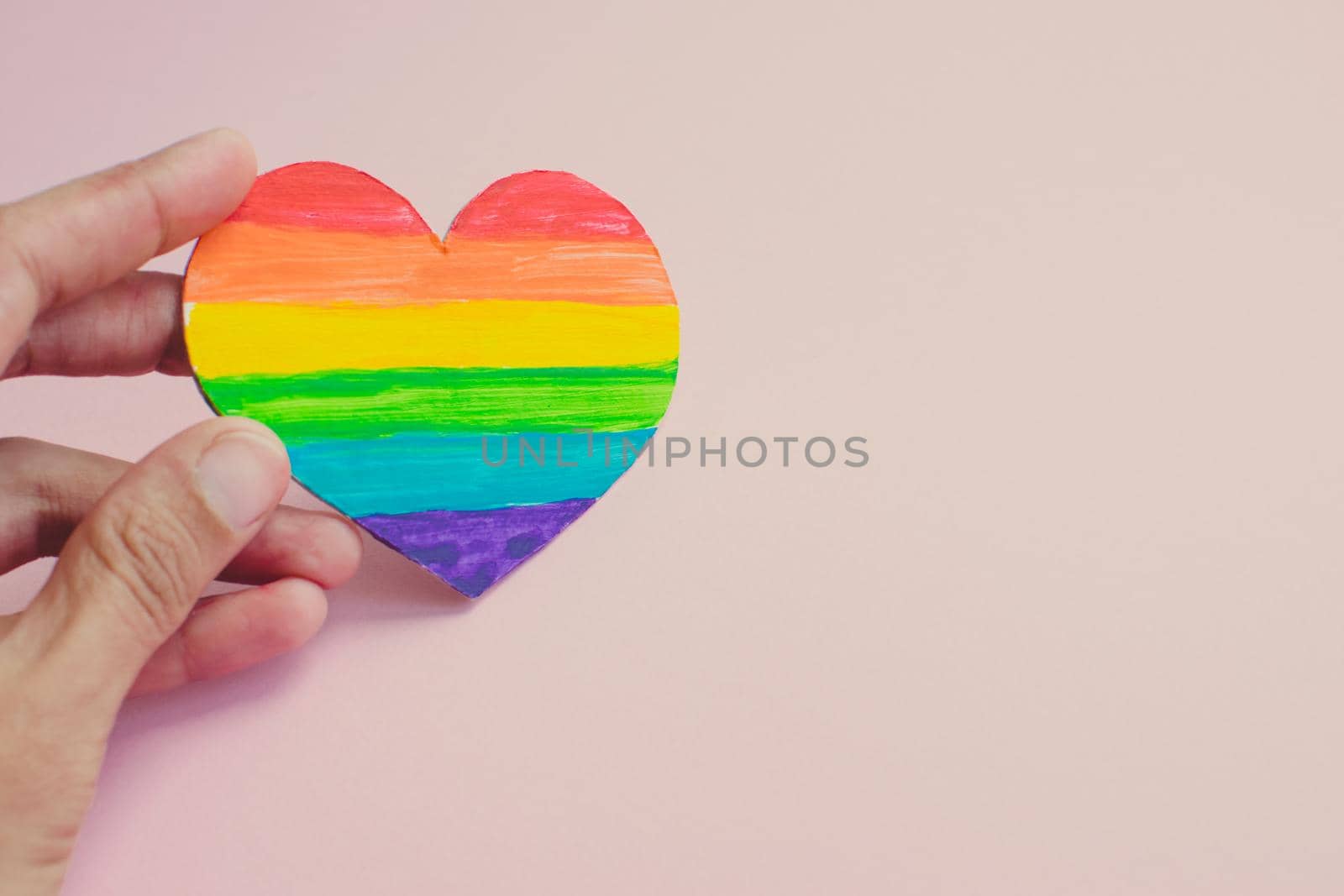 Female hands holding heart with rainbow stripes on pink background. LGBT pride flag, symbol of lesbian, gay, bisexual, transgender, social movements. Homosexual love, Human rights concept. Copy space.