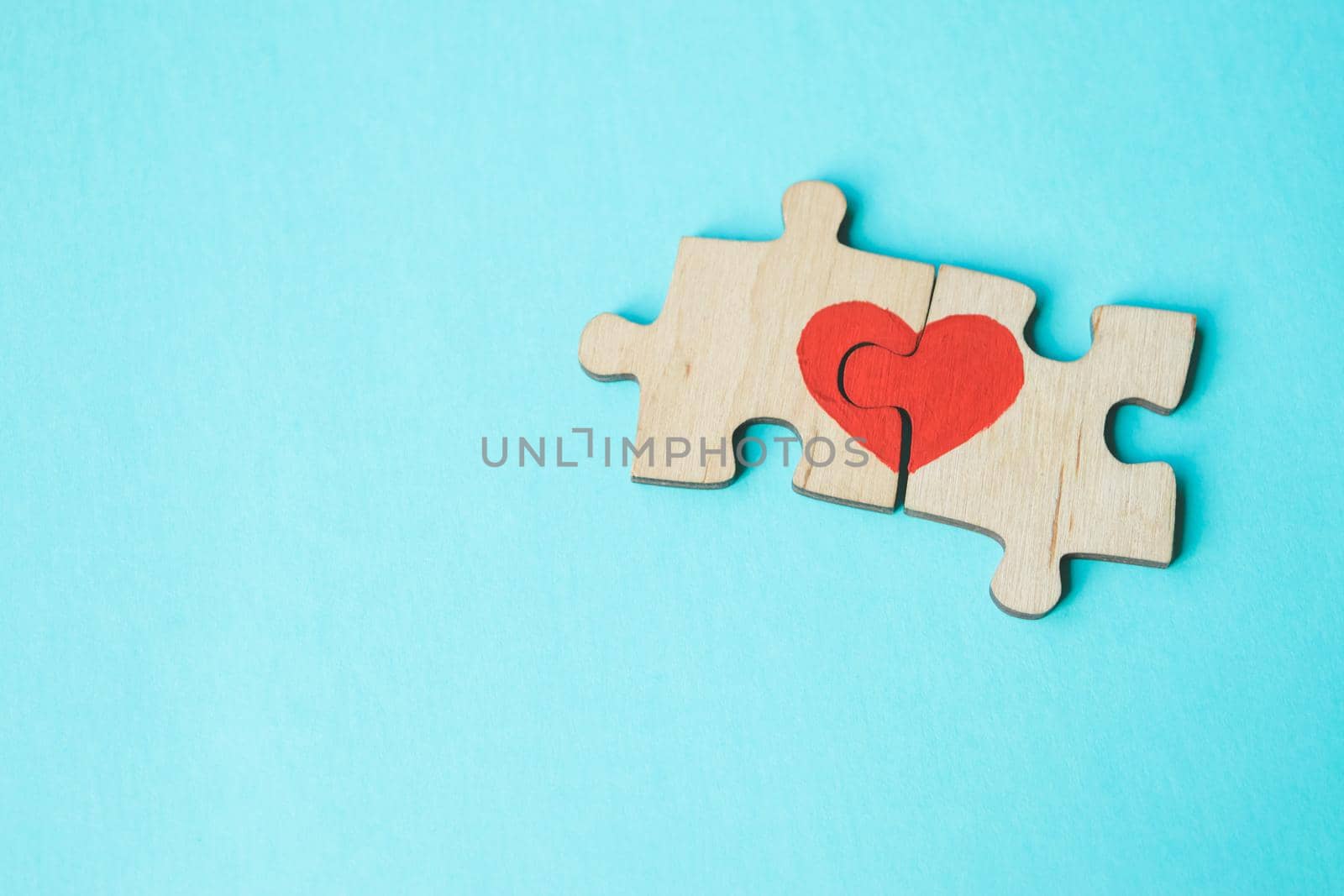 Red heart is drawn on the pieces of the wooden puzzle lying next to each other on blue background. Love concept. St. Valentine day. Reconciliation. Reunion concept. Free space for text