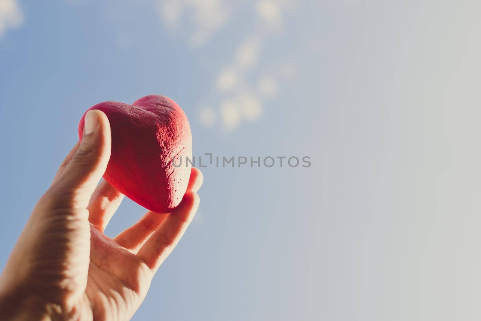 Hand holding the red decorative heart against the blue sky. Day of donor. Love concept. Copy space