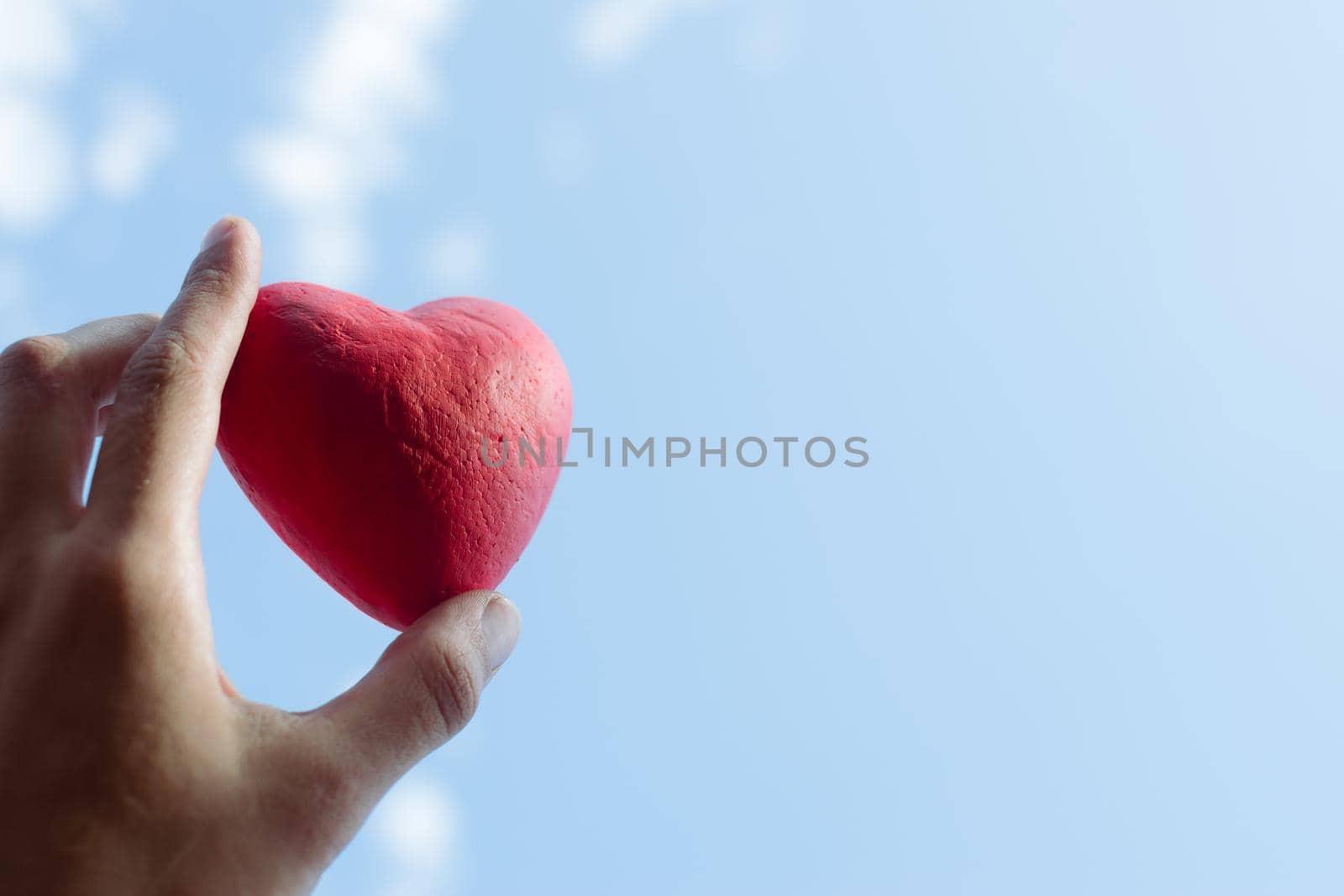 Hand holding the red decorative heart against the blue sky. Day of donor. Love concept