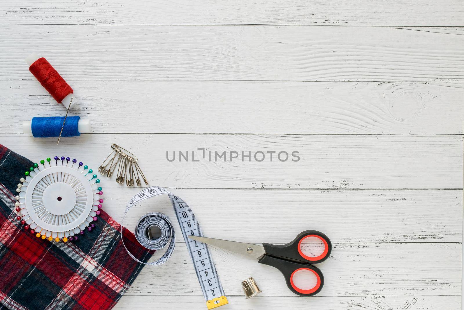 Sewing accessories. Plaid fabric on a white wooden background. Fabric, sewing threads, needle, pins, scissors and sewing centimeter. Copyspace