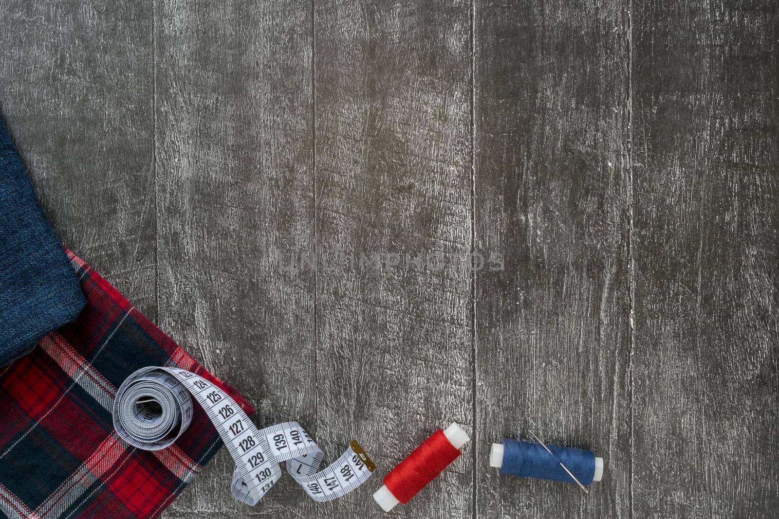 Sewing accessories, denim and plaid fabric on a dark wooden background. Fabric, threads, zipper, needle, buttons and sewing centimeter.