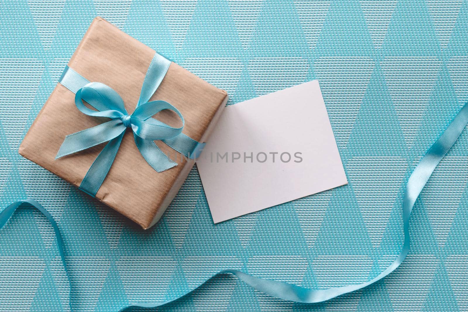 Gift box with blue ribbon on blue background wih greeting card.