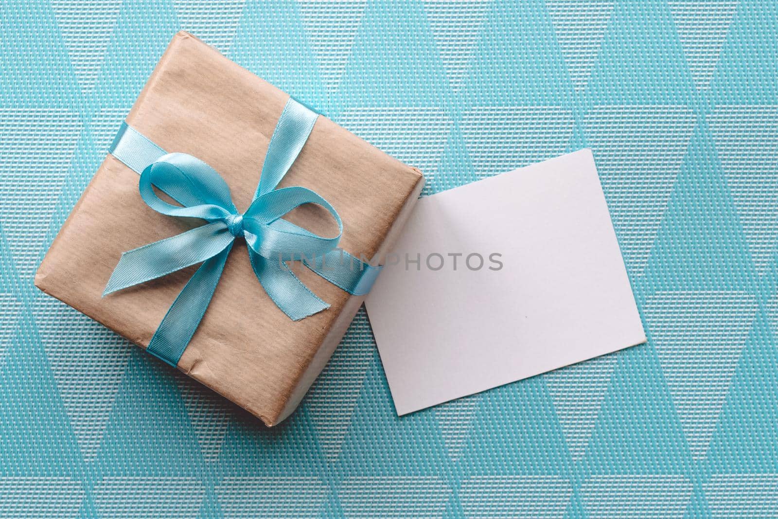 Gift box with blue ribbon on blue background wih greeting card.