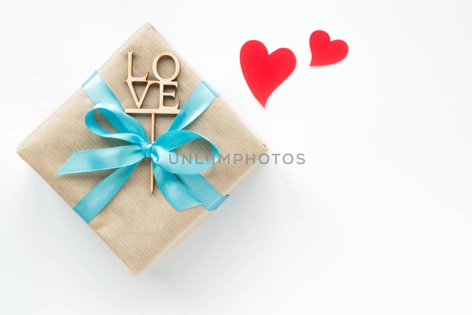 Gift box wrapped in brown paper with blue ribbon on white background. Top view. Flat lay