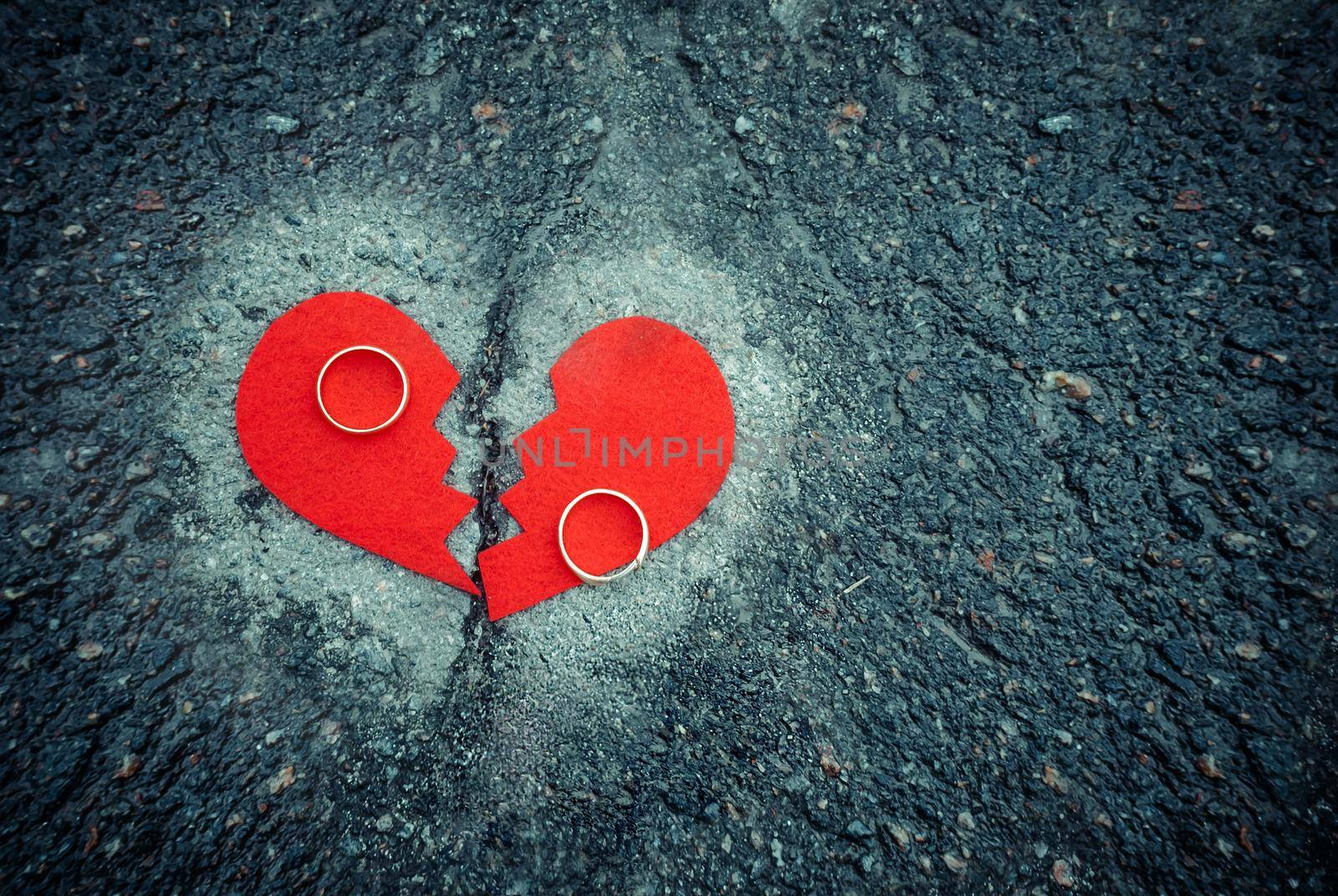 Divorce concept - broken red heart with wedding rings on cracked asphalt. Toned