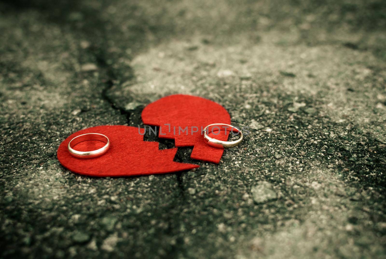 divorce concept - wedding rings on red broken heart on cracked asphalt
