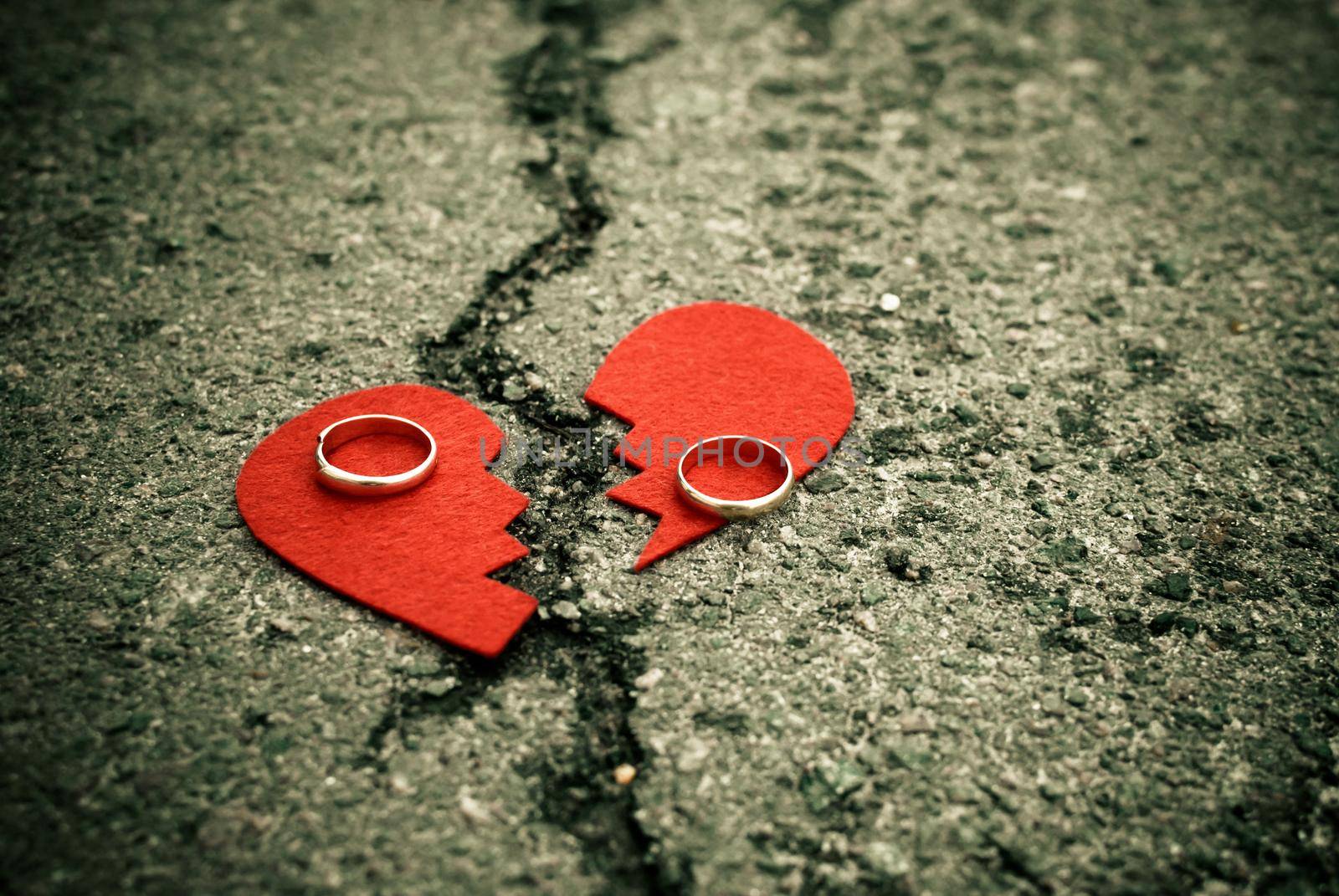 divorce concept - broken heart with wedding rings on cracked asphalt