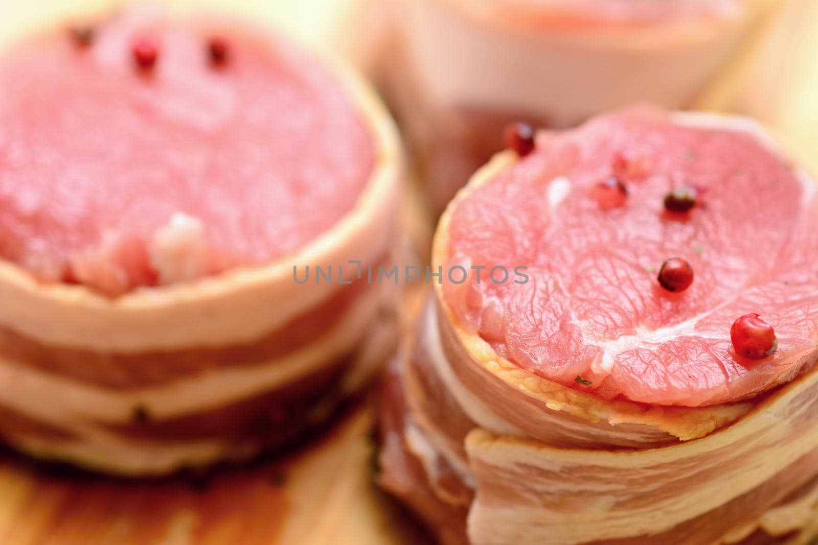 Closeup of fresh raw bacon wrapped pork tenderloin medallions sprinkled with whole red pepper.