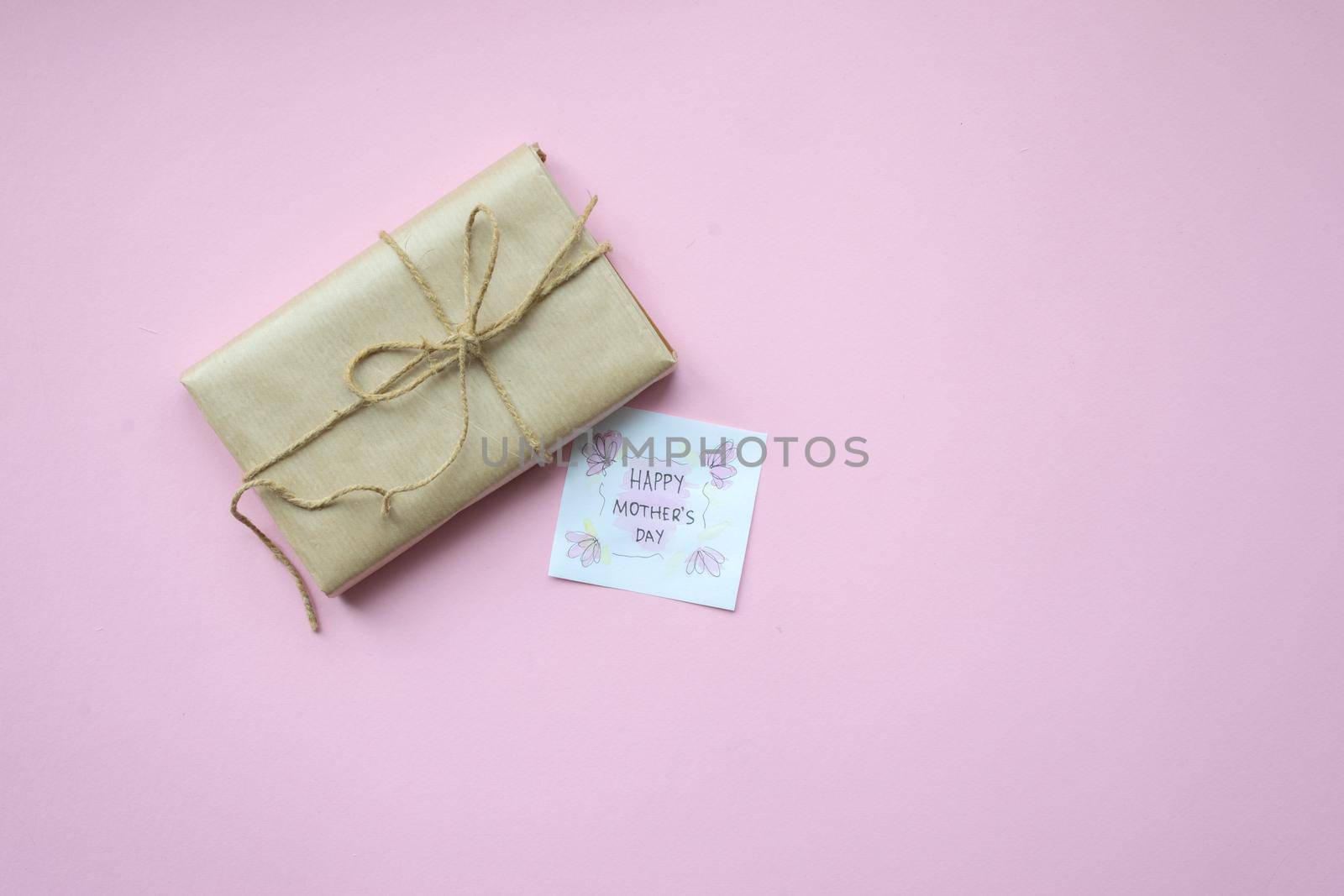 Presents wrapped in brown craft paper and tie hemp string on Light pink background. Gift box with greetings on Mothers Day. Top view. Copyspace