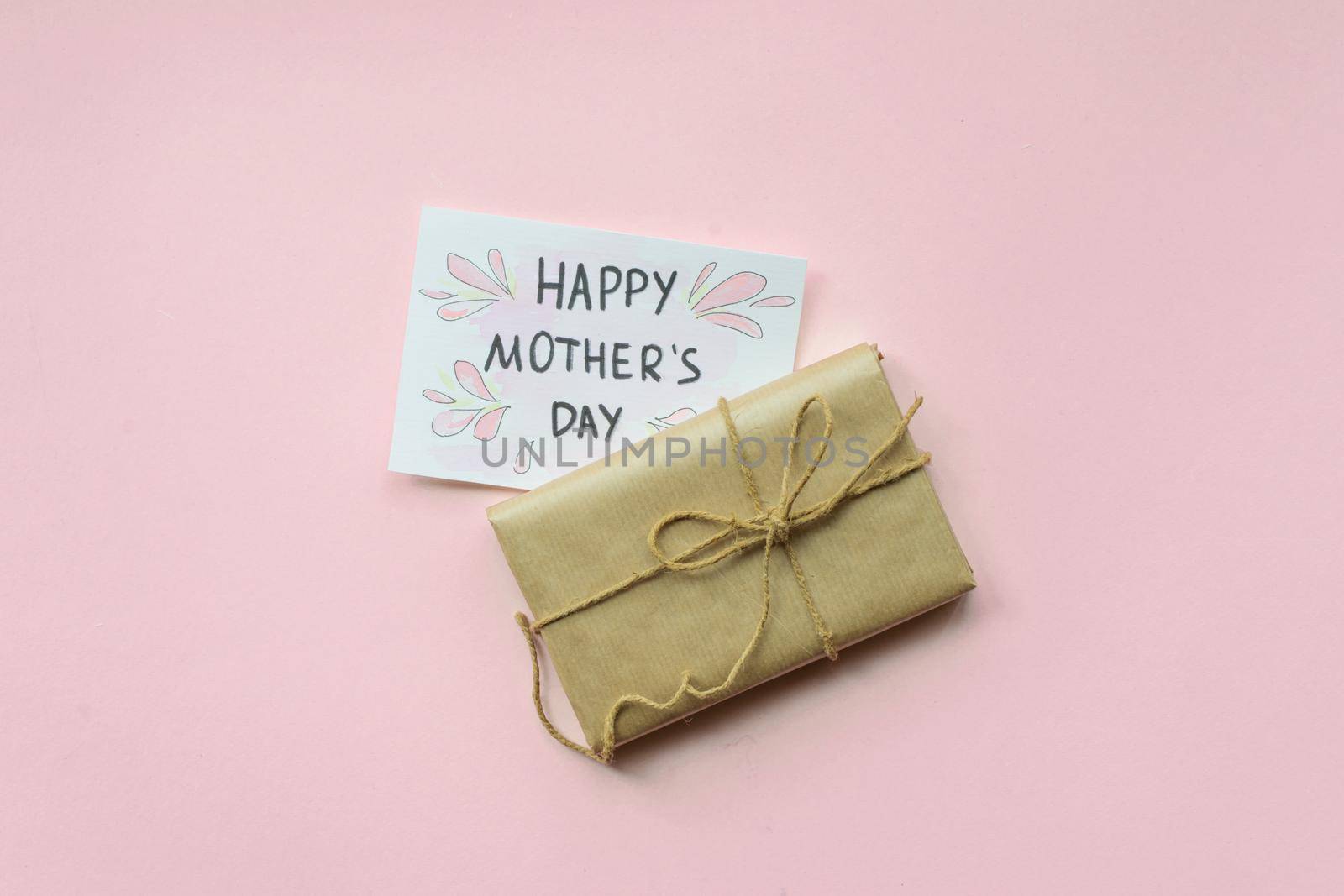 Presents wrapped in brown craft paper and tie hemp string on Light pink background. Gift box with greetings on Mothers Day. Top view. Copyspace