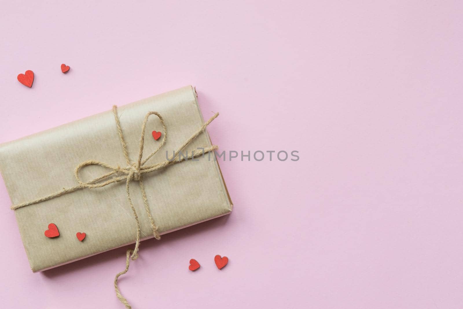 Present wrapped in brown craft paper and tie hemp string on Light pink background. Gift box with decorative red hearts for Mothers Day, Wedding, Birthday and Valentines Day. Top view. Copyspace