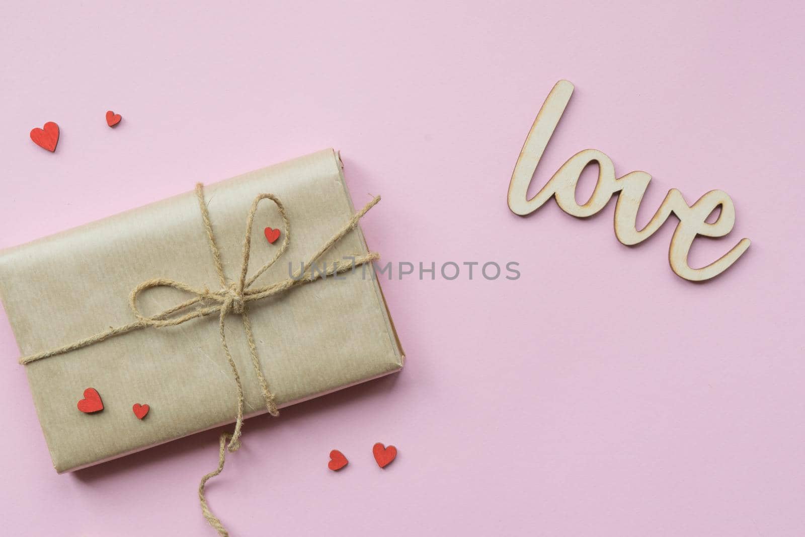 Present wrapped in brown craft paper and tie hemp string on Light pink background. Gift box with decorative red hearts for Mothers Day, Wedding, Birthday and Valentines Day. Top view. Copyspace