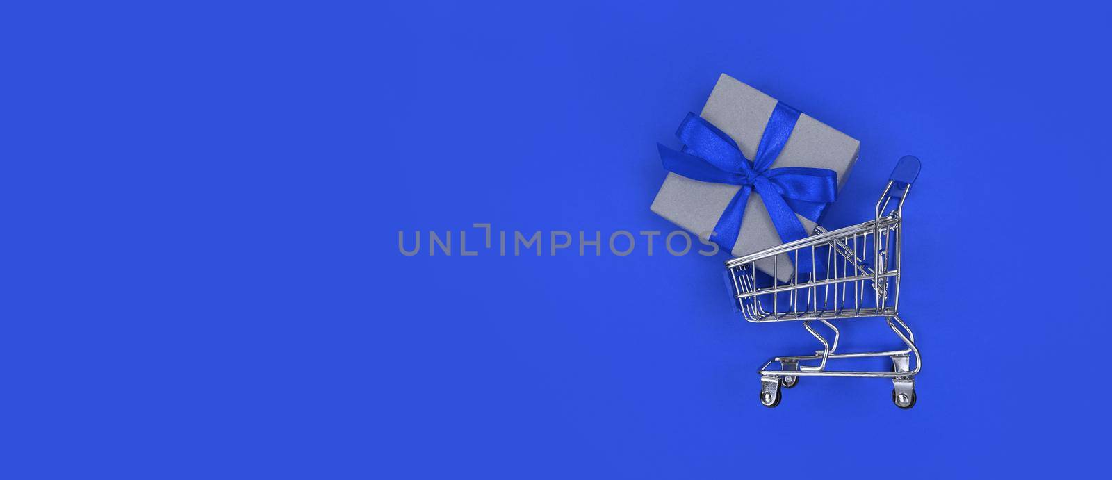 Supermarket trolley and gift box on a blue background with copy space. Shopping concept.