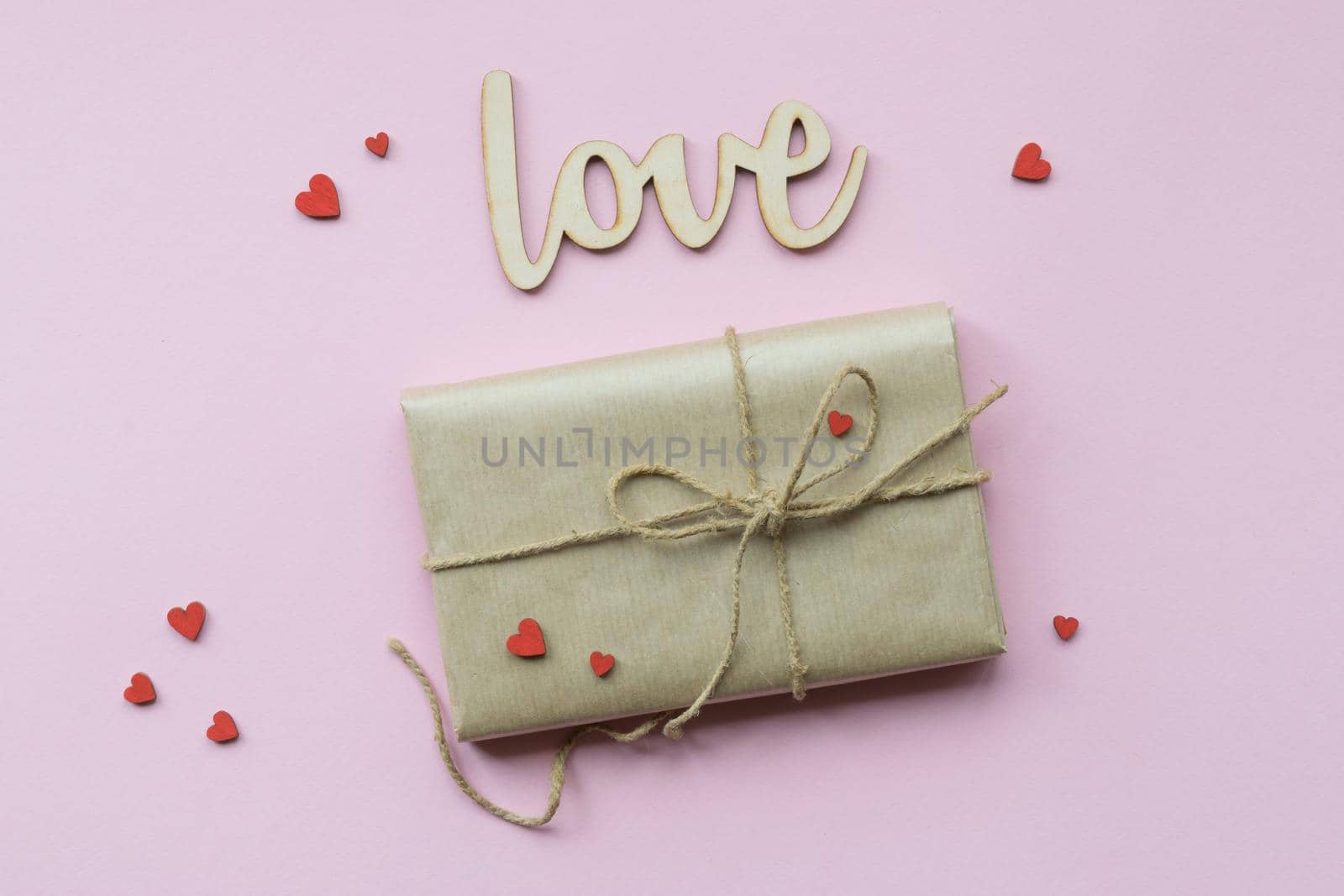 Present wrapped in brown craft paper and tie hemp string on Light pink background. Gift box with decorative red hearts for Mothers Day, Wedding, Birthday and Valentines Day. Top view. Copyspace