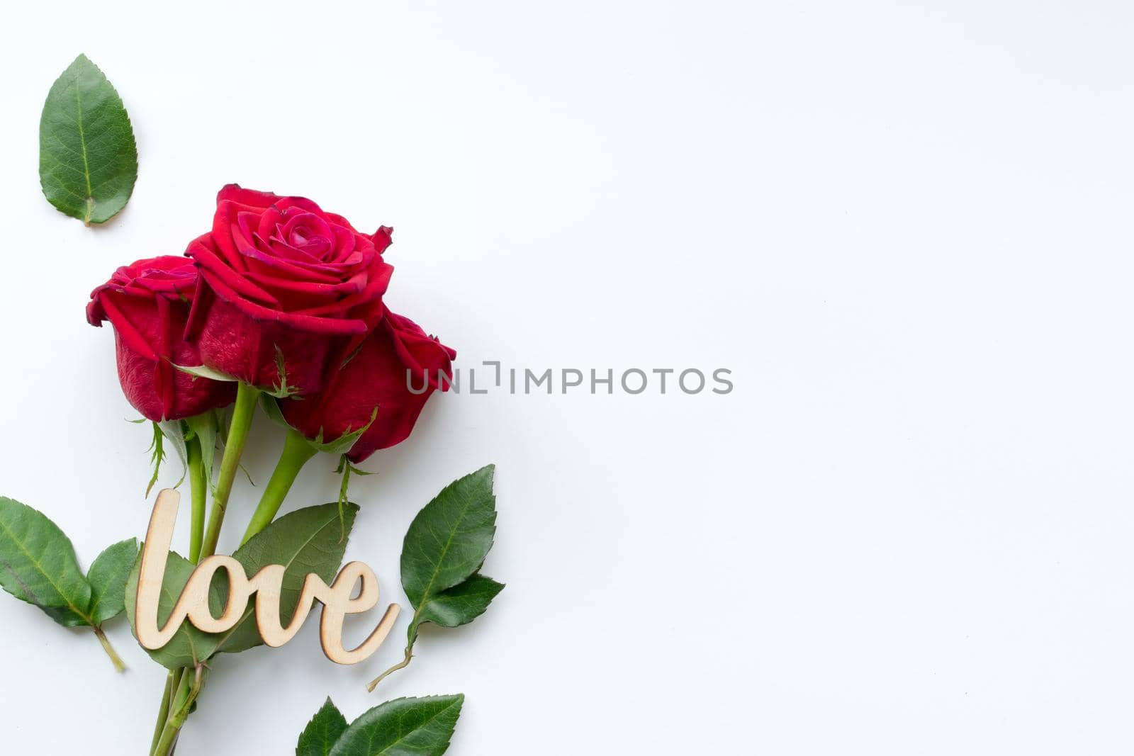 Composition of bouquet of red roses and decorative wooden word love on white background . Happy Valentines Day. Top view. Space for text. Copyspace. Space for text.