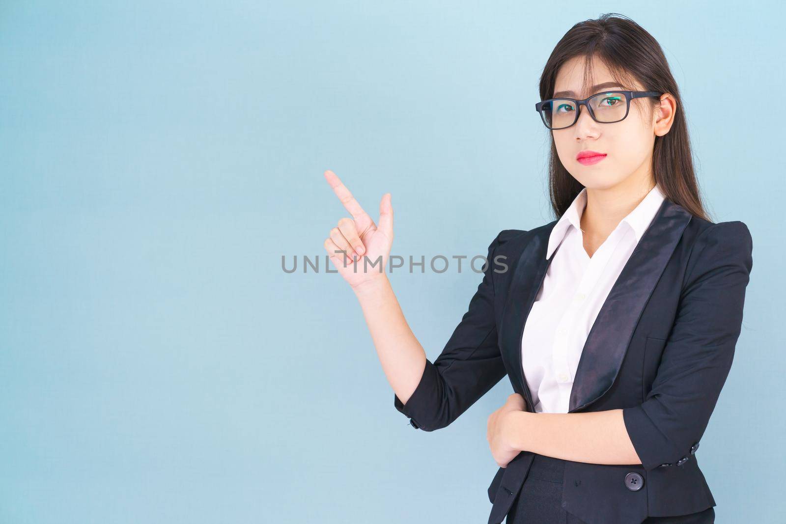 Asian business woman in suit with finger pointing up on blue background