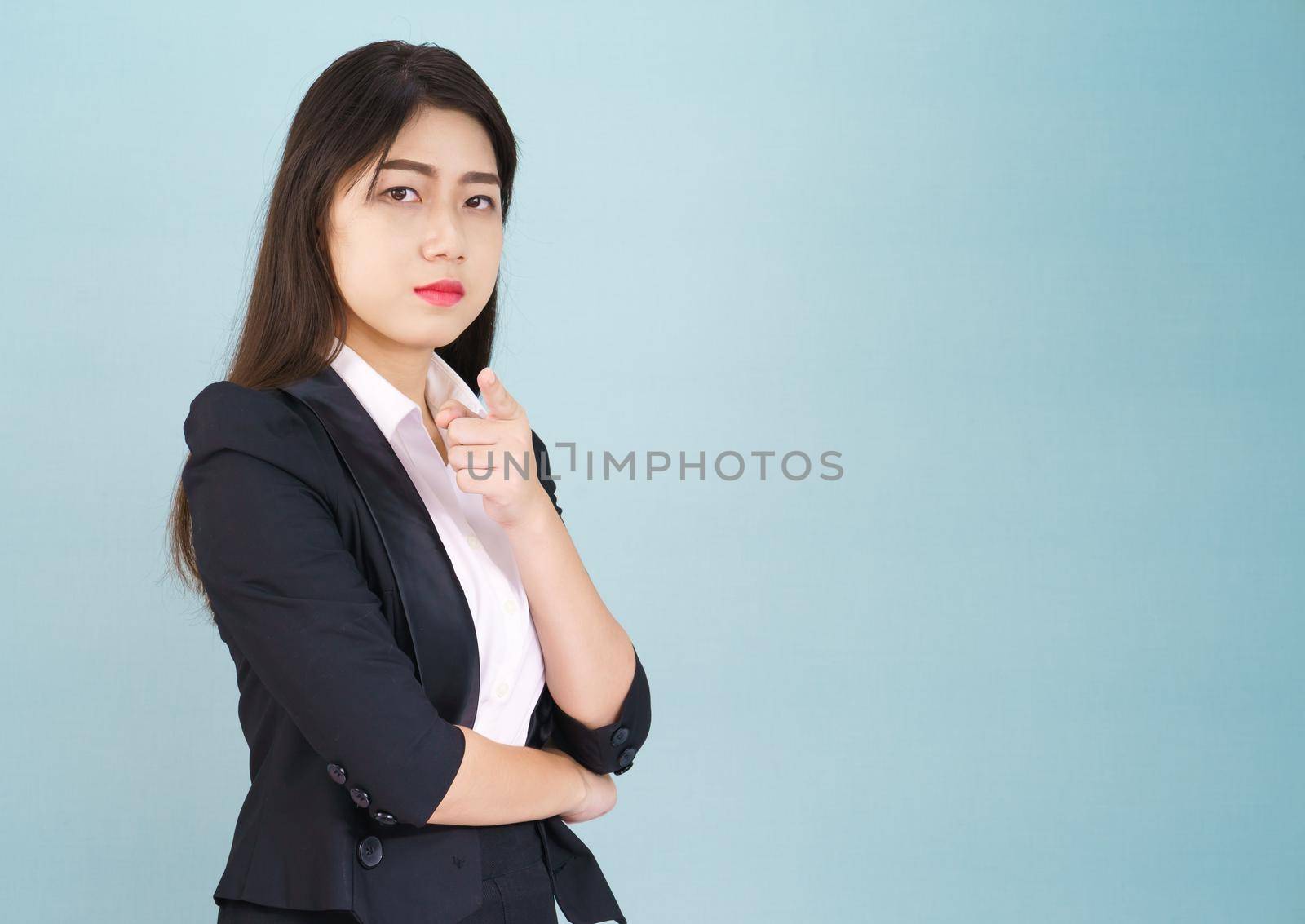 Asian woman looking at camera and pointing finger on blue background