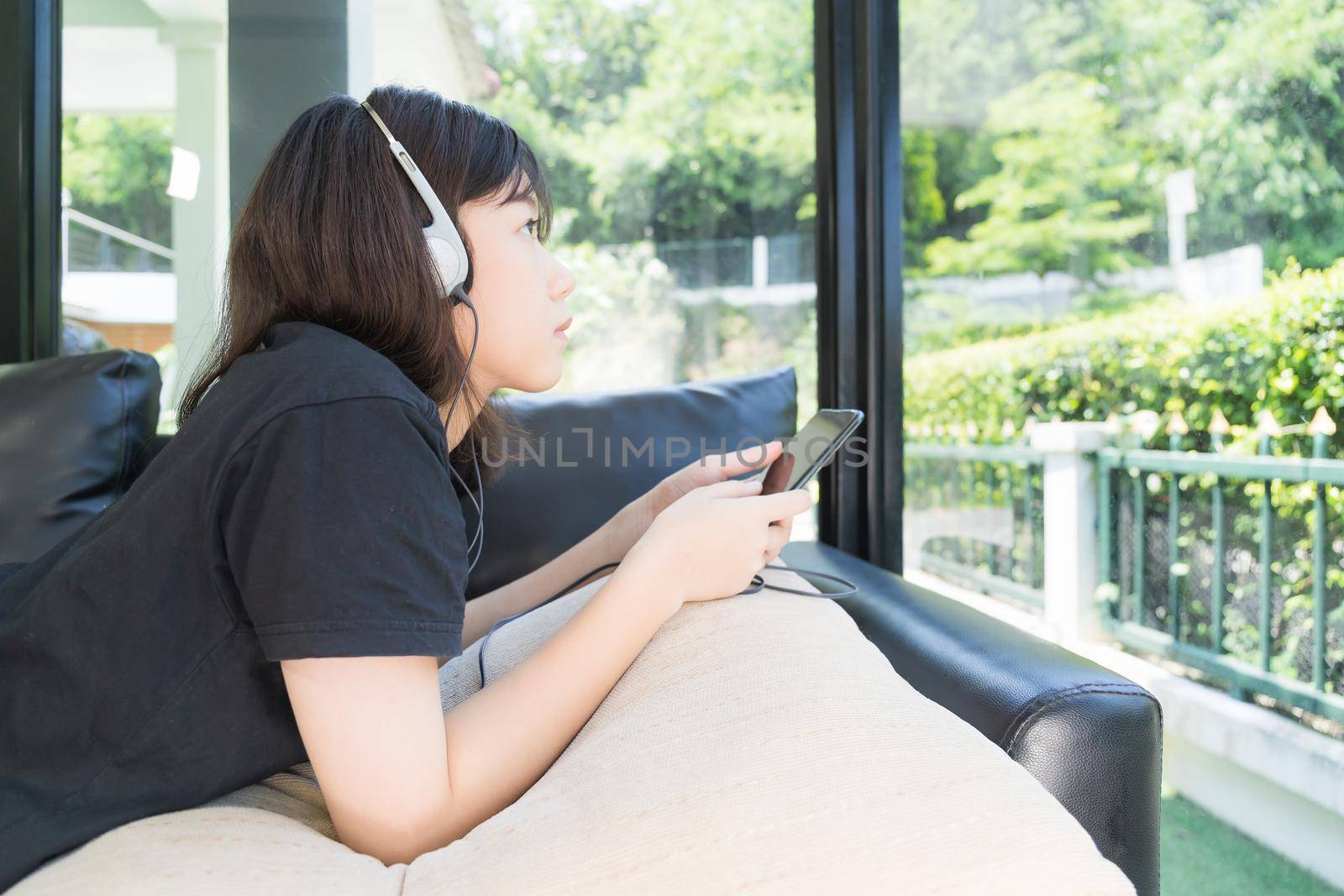 Young girl with headphones and listening to music from mobile phone on the sofa in living room at home