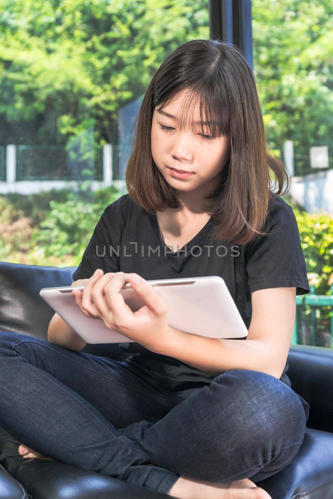 Young girl studying online from digital tablet on the sofa in parlor at home