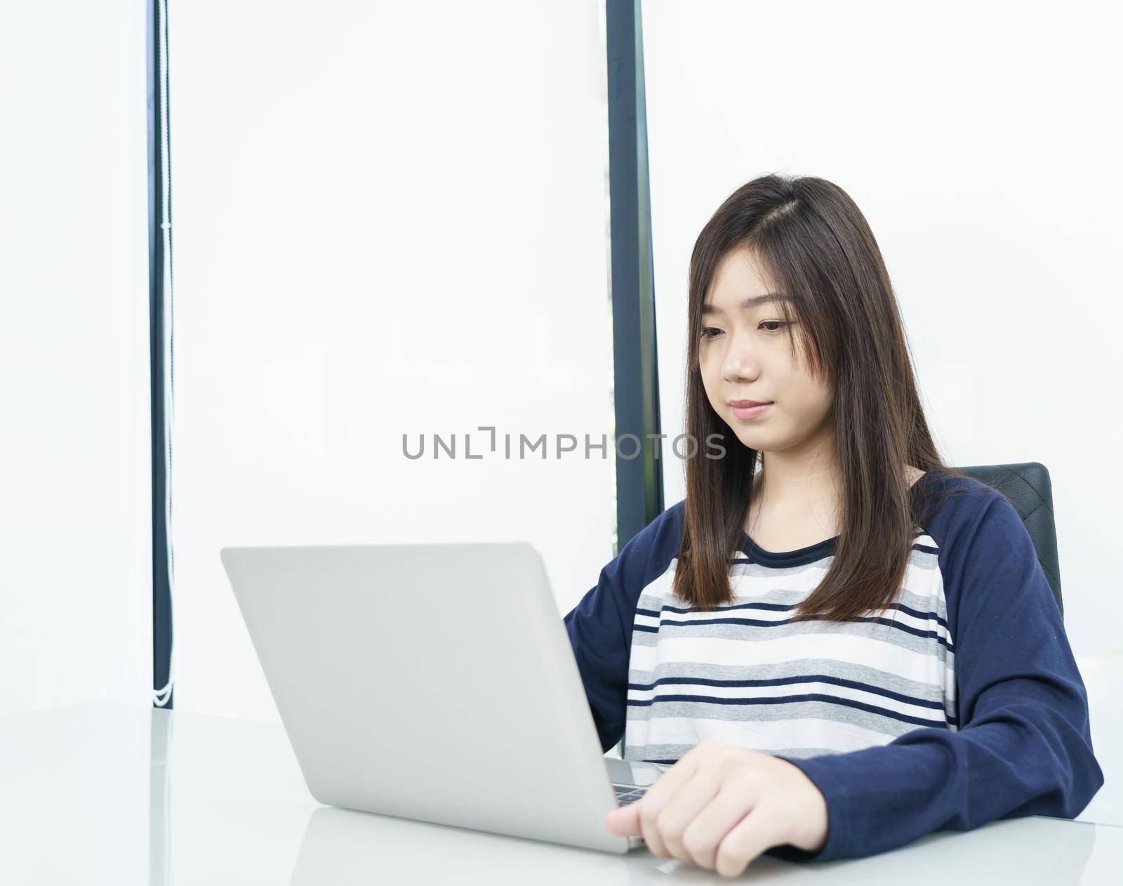 Young female student sitting in living room using laptop at desk learning online