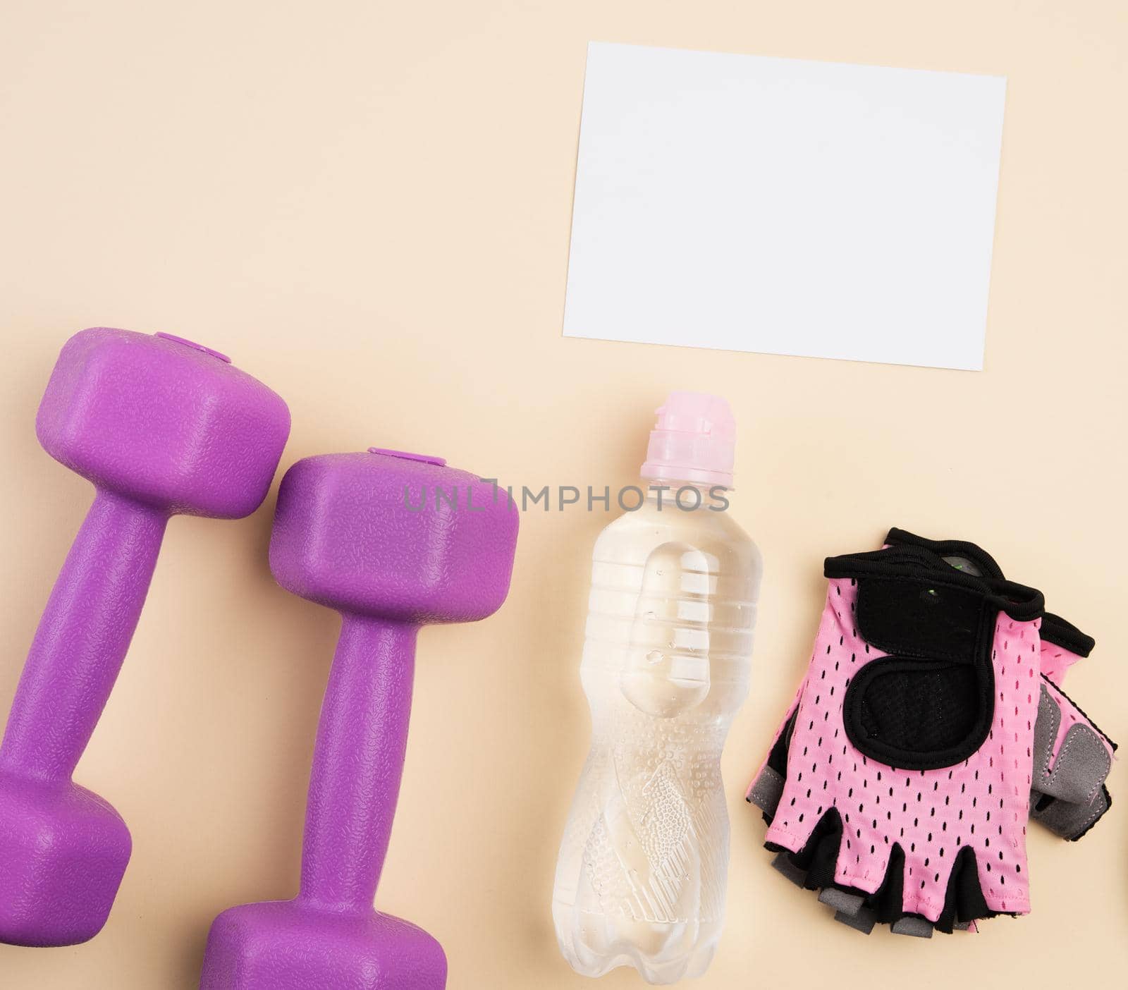 pink sports gloves, pair of purple dumbbells and and bottle of water on a beige background by ndanko