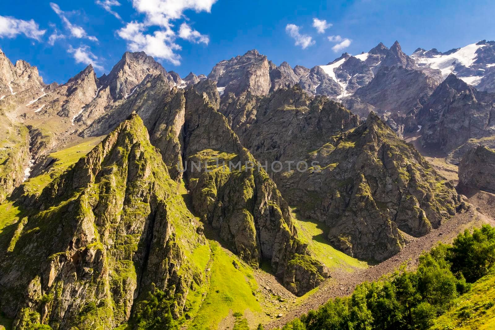 High mountains of the Caucasus with a beautiful view. Green vegetation and shrubs on sharp rocks above a blue sky. Magnificent mesmerizing landscape.