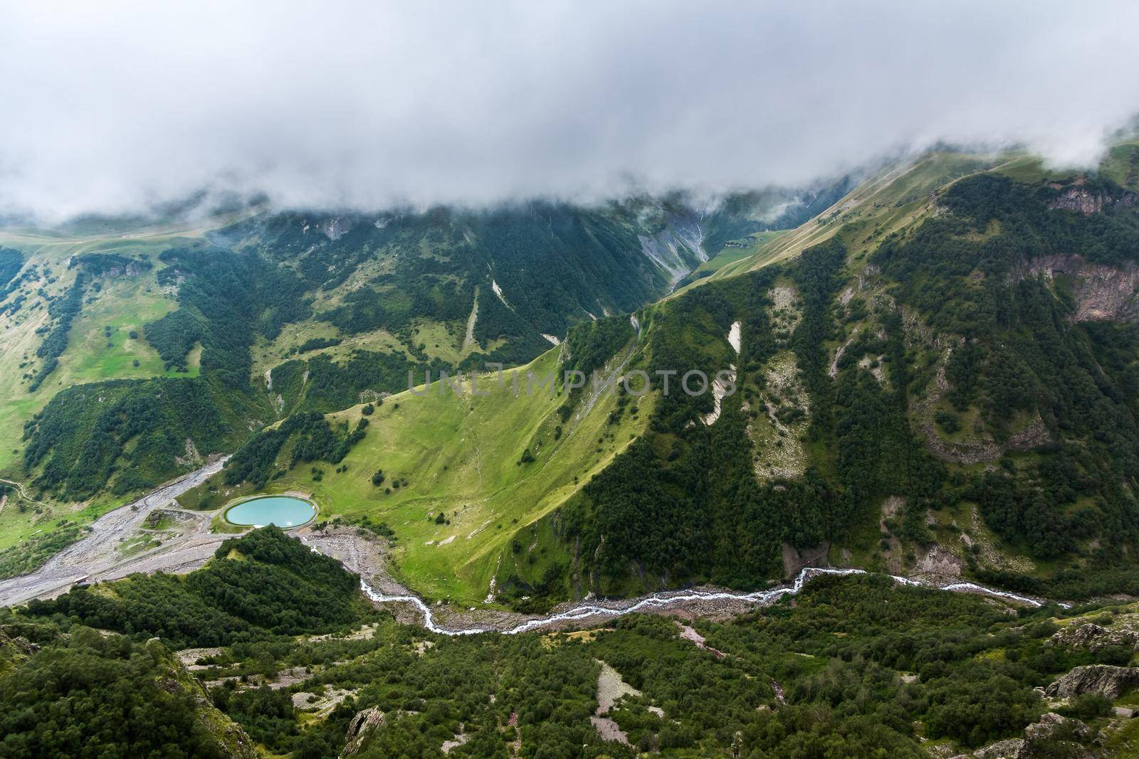High mountains of the Caucasus with a beautiful view. Green vegetation and shrubs on sharp rocks, Between the mountains of the lake into which the river flows. Magnificent mesmerizing landscape.