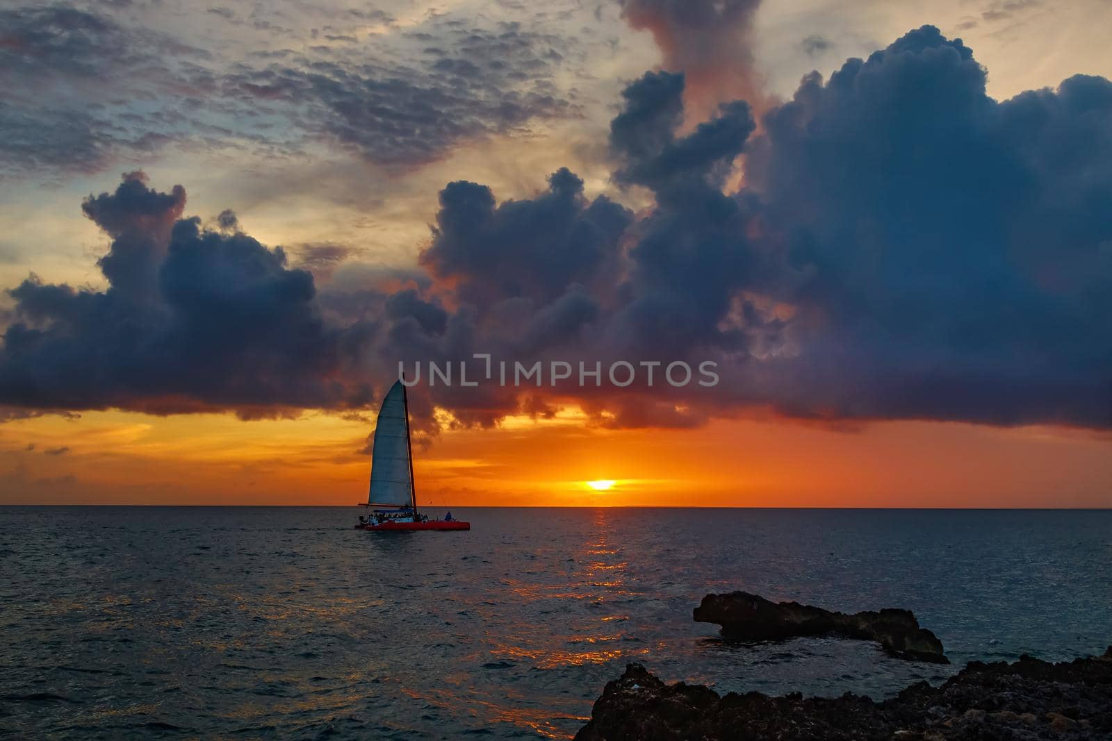 Impressive red-orange sunset on the sea in the distance a sailboat sails against the background of a beautiful sunset sky. The sun sets, seeing off the day with romantic rays
