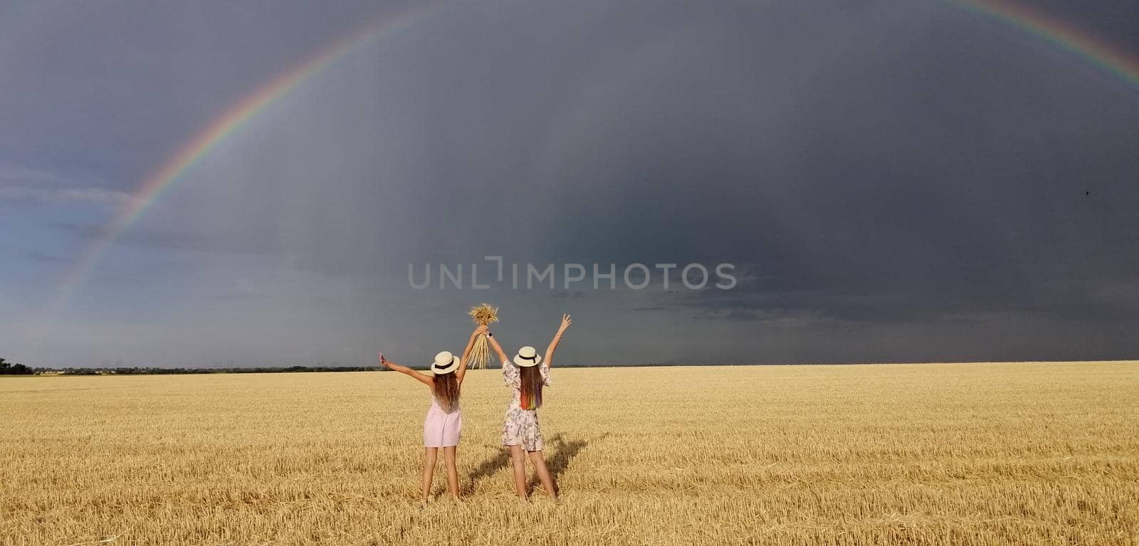 In a wheat field after the rain, two girls run. Colorful real rainbow over the horizon. europe Ukraine. Summer crop fields, ripening wheat field. by ja-aljona