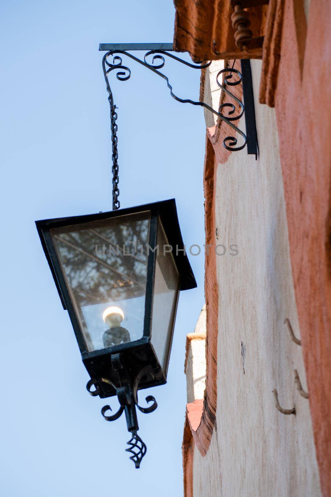 Classic metal and glass lantern hanging from old Hispanic building and under blue sky. Hanging lamp next to house with classic architecture in Mexico City. Traditional outdoors decoration